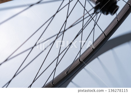 Close-up of a black bicycle rim with metal spokes casting shadows on a light blue surface. 136278115