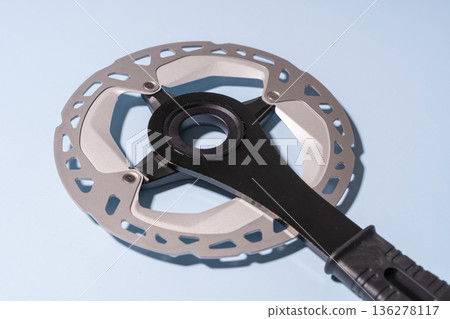 Close-up of a metallic bicycle disc brake rotor attached to a black handle on a blue background Close-up of a metallic bicycle disc brake rotor attached to a black handle on a blue background 136278117