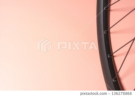 Close-up of a black bicycle rim with thin metal spokes radiating from the hub and casting shadows on a pink background. 136278868