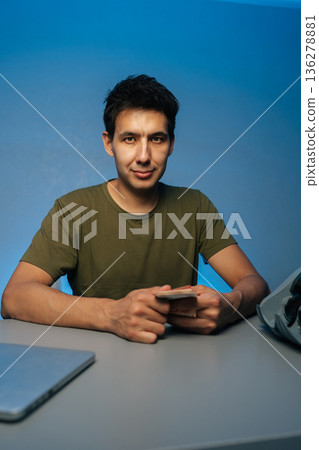 Vertical portrait of handsome cashier counting banknotes sitting at desk, using laptop and money counter machine, on isolated blue background, engaged in financial transactions and cash handling. Vertical portrait of handsome cashier counting banknotes sitting at desk, using laptop and money counter machine, on isolated blue background, engaged in financial transactions and cash handling. 136278881