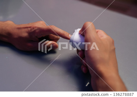 Closeup top view of male hands holding portable electric nail clipper, filing nails on gray table while performing manicure at home using modern beauty tools for effortless grooming and self-care. 136278887