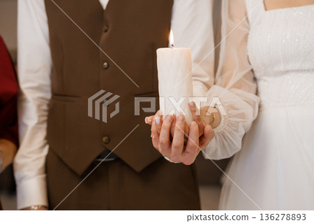 Elegant wedding couple holding a lit white candle together in a warm, intimate ceremony moment Elegant wedding couple holding a lit white candle together in a warm, intimate ceremony moment 136278893