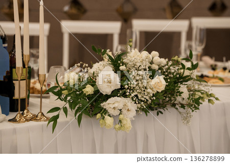 Elegant White Floral Centerpiece with Greenery and Gold Candle Holders on Wedding Table Setting Elegant White Floral Centerpiece with Greenery and Gold Candle Holders on Wedding Table Setting 136278899