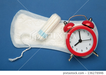 Alarm clock with sanitary female tampons and menstrual sanitary pads. Medical concept of woman critical days and menstruation. Alarm clock with sanitary female tampons and menstrual sanitary pads. Medical concept of woman critical days and menstruation. 136278946