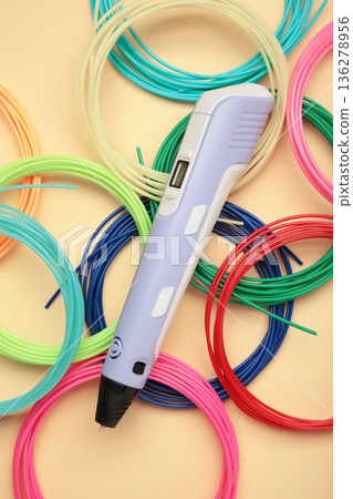 Children's 3D handle with plastic coils red, white, yellow, blue on beige background. Plastic PLA and ABS filament material for printing on a 3D pen Children's 3D handle with plastic coils red, white, yellow, blue on beige background. Plastic PLA and ABS filament material for printing on a 3D pen 136278956