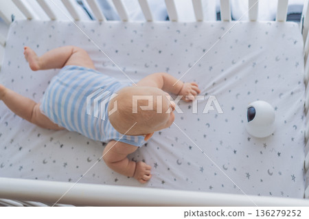 Baby monitor camera placed inside a crib where an infant is lying, ensuring safety and constant supervision. Modern parenting scene combining care and technology. Baby monitoring, security and smart 136279252