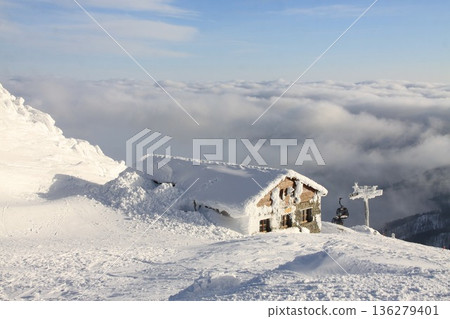Snow-covered alpine mountain hut nestled on a high ridge. 136279401
