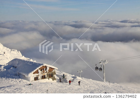 Snow-covered alpine mountain hut nestled on a high ridge. 136279402