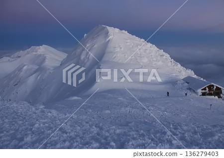 a snow covered mountain peak at dusk, with a dark blue and pink sky and a small mountain hut. a snow covered mountain peak at dusk, with a dark blue and pink sky and a small mountain hut. 136279403