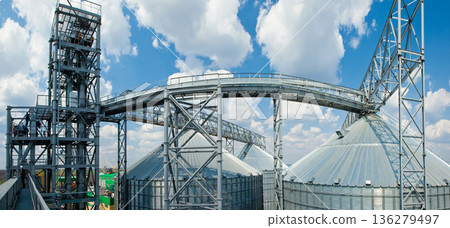 Wide panoramic view of a modern industrial grain terminal with silver silos under a blue sky Wide panoramic view of a modern industrial grain terminal with silver silos under a blue sky 136279497