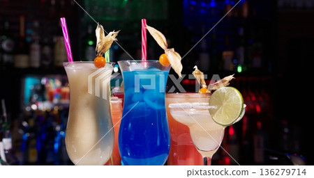 Colorful cocktails sit on a bar counter at a lively bar during the evening 136279714