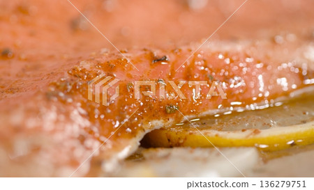 Fresh salmon fillet being prepared with spices and lemon slices on a cutting board before cooking 136279751
