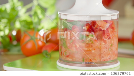Chopping tomatoes and herbs in a food processor on a kitchen table with vegetables around Chopping tomatoes and herbs in a food processor on a kitchen table with vegetables around 136279761