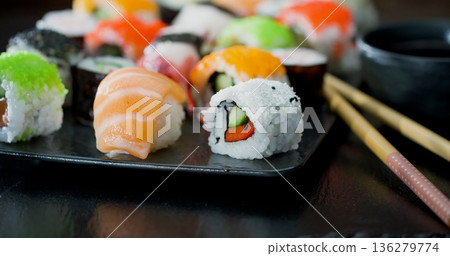 Variety of sushi served on a black plate with chopsticks in a Japanese restaurant during lunch hours Variety of sushi served on a black plate with chopsticks in a Japanese restaurant during lunch hours 136279774