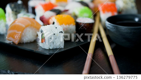 Sushi rolls are arranged on a black plate with chopsticks placed beside them at a dining table Sushi rolls are arranged on a black plate with chopsticks placed beside them at a dining table 136279775