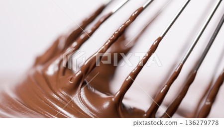 Whisk mixes melted chocolate in a bowl during dessert preparation in a kitchen setting 136279778
