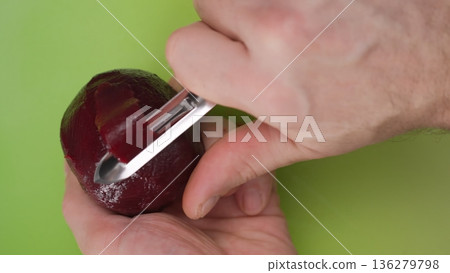 Hands peel a beet on a green cutting board with a vegetable peeler in a kitchen setting during the day Hands peel a beet on a green cutting board with a vegetable peeler in a kitchen setting during the day 136279798