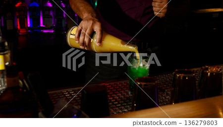 Bartender pours colorful drink into glass during busy night at the bar with bright lights Bartender pours colorful drink into glass during busy night at the bar with bright lights 136279803