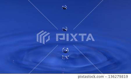 Water droplets falling in blue background creating ripples in calm liquid surface 136279819