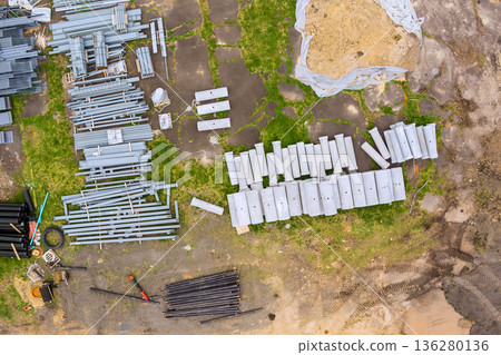 Metal beams pipes are arranged on ground at construction site with some grass dirt 136280136