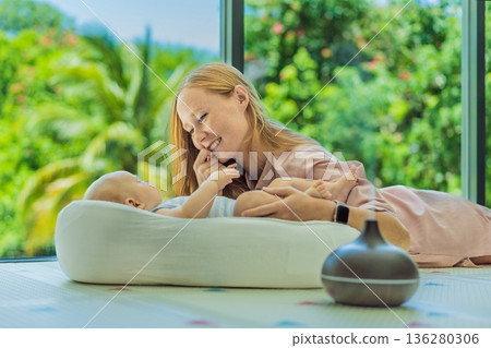 Newborn baby resting in a cozy cocoon beside mother with aroma lamp, calm home atmosphere. Infant relaxation, gentle care, motherhood routine, aromatherapy for babies and family wellbeing concept. Newborn baby resting in a cozy cocoon beside mother with aroma lamp, calm home atmosphere. Infant relaxation, gentle care, motherhood routine, aromatherapy for babies and family wellbeing concept. 136280306