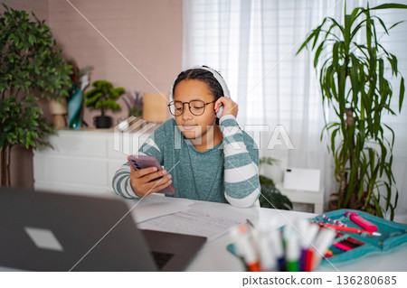 Girl student listening to music using smartphone and headphones while studying 136280685