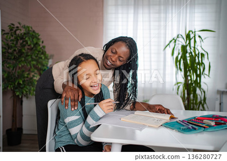 Mother helping daughter with homework, laughing and smiling Mother helping daughter with homework, laughing and smiling 136280727