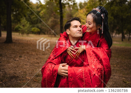 Intercultural couple embracing in traditional red wedding attire outdoors 136280786