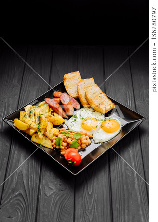 Full breakfast plate with fried eggs, sausages, potatoes, beans and toast on dark table Full breakfast plate with fried eggs, sausages, potatoes, beans and toast on dark table 136280797