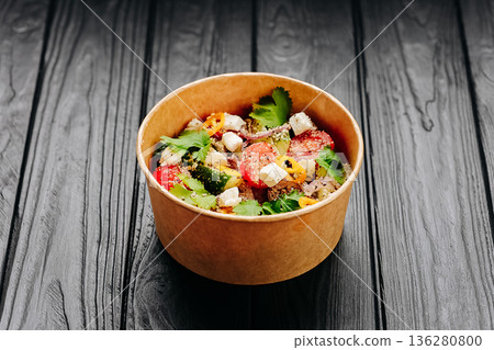 Fresh vegetable salad with feta and herbs in kraft takeaway bowl on dark wooden table 136280800