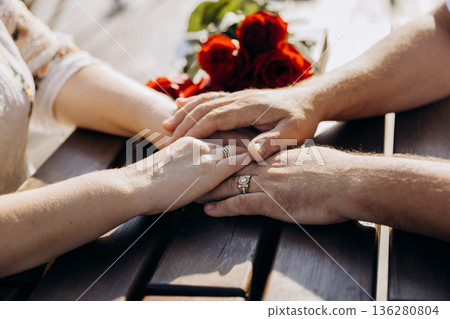 Wedding rings on intertwined hands with red roses, romantic closeup of couple, copy space 136280804