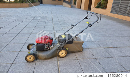 Outdoor maintenance with push lawnmower on paved surface in courtyard setting Outdoor maintenance with push lawnmower on paved surface in courtyard setting 136280944