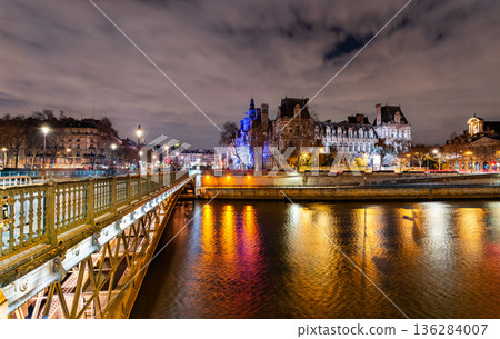 Pont d'Arcole bridge crosses the Seine river leading to the illuminated Hotel de Ville city hall building during the evening in Paris, France 136284007