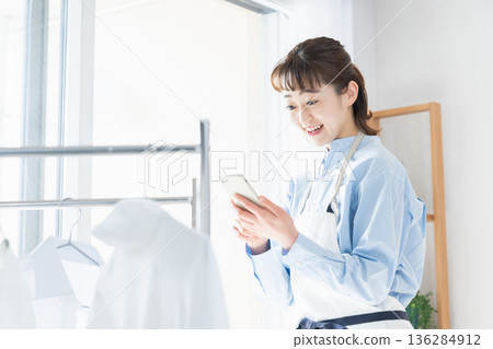 A young woman looking at her smartphone while doing housework 136284912