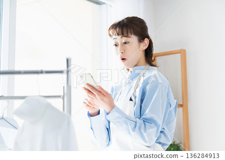 A young woman looking at her smartphone while doing housework 136284913
