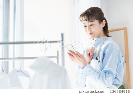A young woman looking at her smartphone while doing housework A young woman looking at her smartphone while doing housework 136284916
