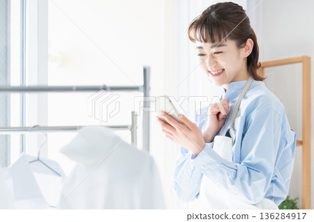 A young woman looking at her smartphone while doing housework A young woman looking at her smartphone while doing housework 136284917