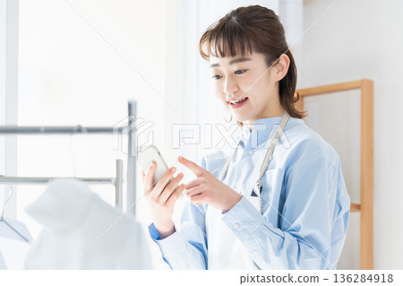 一位年輕女子一邊做家事一邊看智慧型手機 一位年輕女子一邊做家事一邊看智慧型手機 136284918