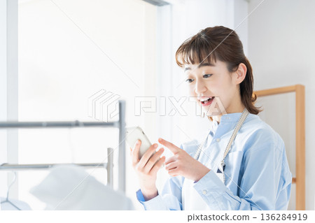 一位年輕女子一邊做家事一邊看智慧型手機 136284919