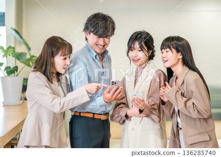 A businessman and a businesswoman smiling and talking while looking at their smartphones 136285740