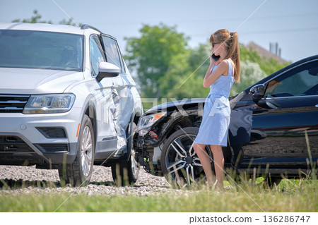 Sad female driver speaking on sellphone on street side calling for emergency service after car accident. Road safety and insurance concept 136286747