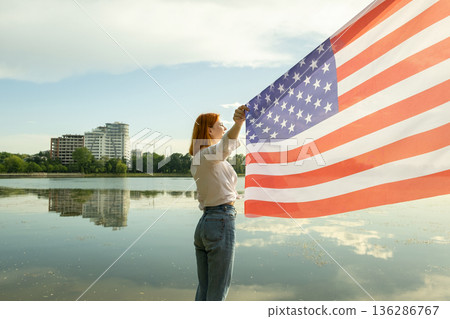 Happy red haired young woman with United States national flag in her hand. Positive girl celebrating US independence day. 136286767
