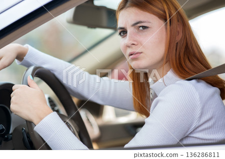 Sad tired yound woman driver sitting behind the car steering wheel in traffic jam. Sad tired yound woman driver sitting behind the car steering wheel in traffic jam. 136286811