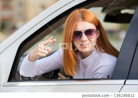 Closeup portrait of pissed off displeased angry aggressive woman driving a car shouting at someone with finger to temple gesture. 136286812