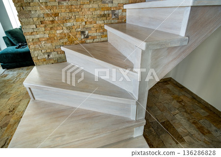 Stylish wooden contemporary staircase inside loft house interior. Modern hallway with decorative limestone brick walls and white oak stairs. 136286828