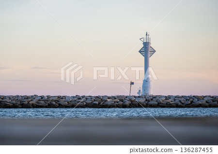 Minimal Lighthouse on Breakwater at Calm Sea and Pastel Sky 136287455