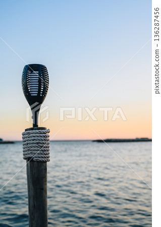 Outdoor Torch on Wooden Post by Sea at Sunset 136287456