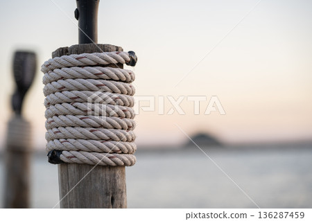Rope Wrapped Around Wooden Post by Calm Sea at Sunset Rope Wrapped Around Wooden Post by Calm Sea at Sunset 136287459