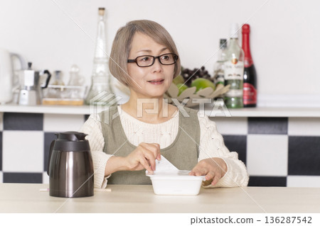 Senior woman pouring hot water into cup noodles in the kitchen Senior woman pouring hot water into cup noodles in the kitchen 136287542