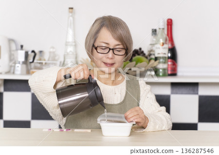 廚房裡,一位老婦人正往杯麵倒熱水。 廚房裡,一位老婦人正往杯麵倒熱水。 136287546
